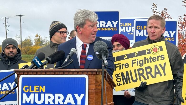 A man wearing a suit is speaking at a podium with a sign saying 