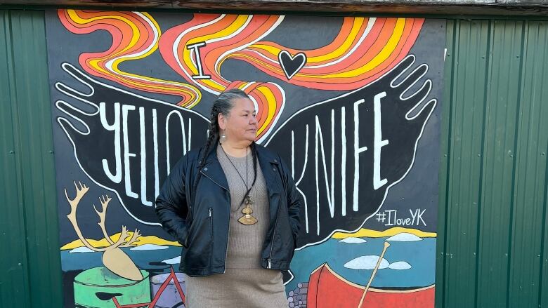 A woman poses in front of a painted mural.