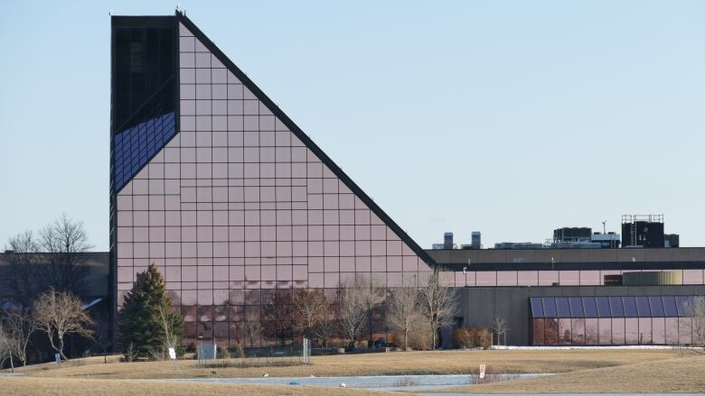 A large glass-fronted building, with one sharply slanted side, is shown in a wide shot on a spring day.