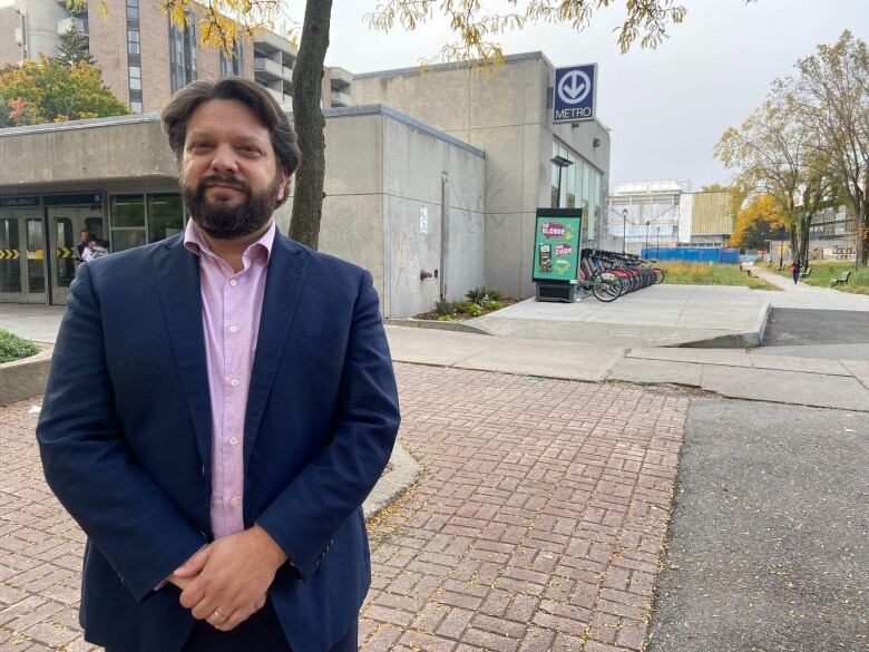 ric Caldwell in front of a Montreal Metro station wearing a pink shirt and navy jacket.