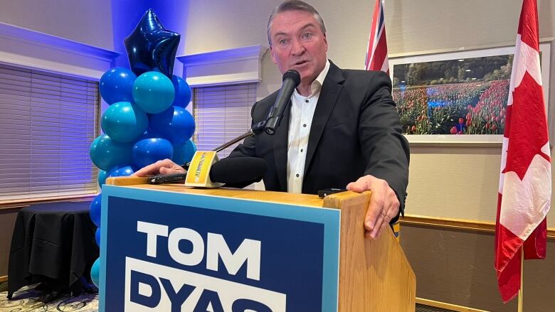 A man in black suit stands behind a podium and speaks.