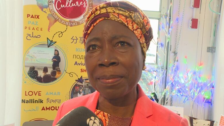 A women wearing a yellow and burgundy headwrap speaks with a CBC reporter.