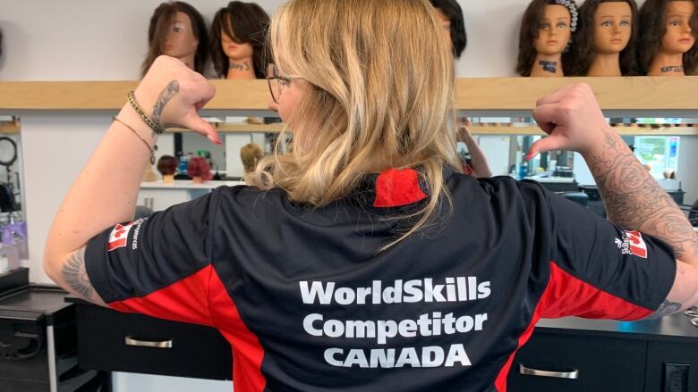 A woman stands back on, wearing a shirt that reads: World Skills Competitor, Canada.