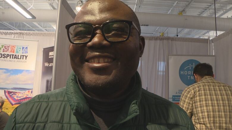 A smiling bald man wearing glasses and a green jacket speaks with a CBC reporter.