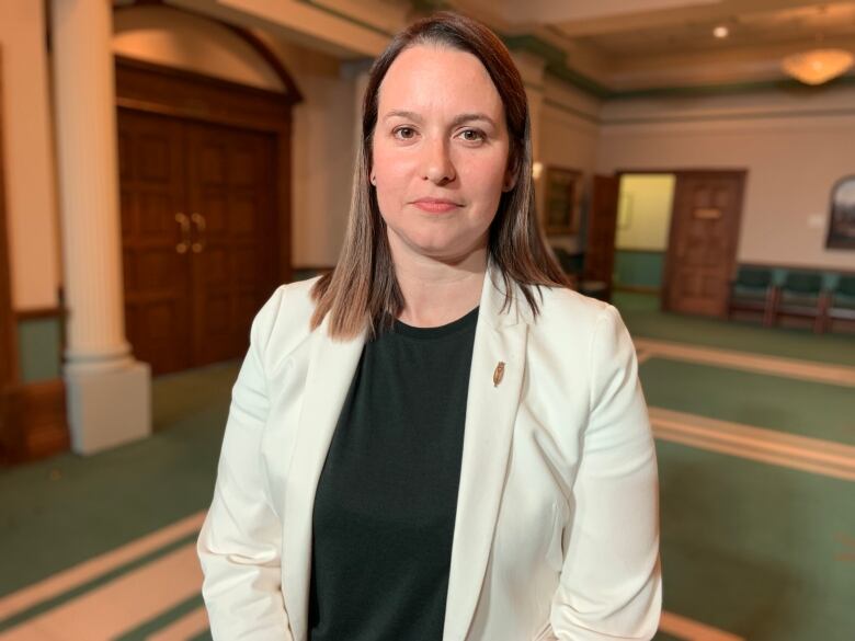 A woman stands in the scrum area of Confederation Building in St. John's. She wears a white blazer with a dark green shirt.