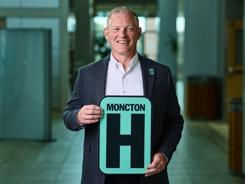 A man stands centre wearing a suit. He holds a sign that says 