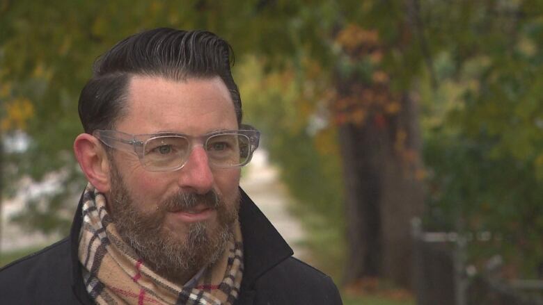 A man wearing glasses and a scarf is talking to someone out of frame.