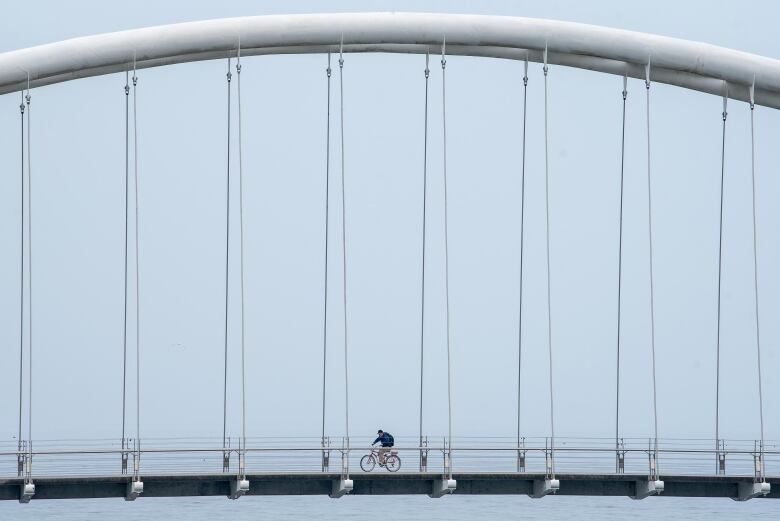 A cyclist rides across the Humber Bay Arch Bridge in Toronto, on an overcast day on July 5, 2022.