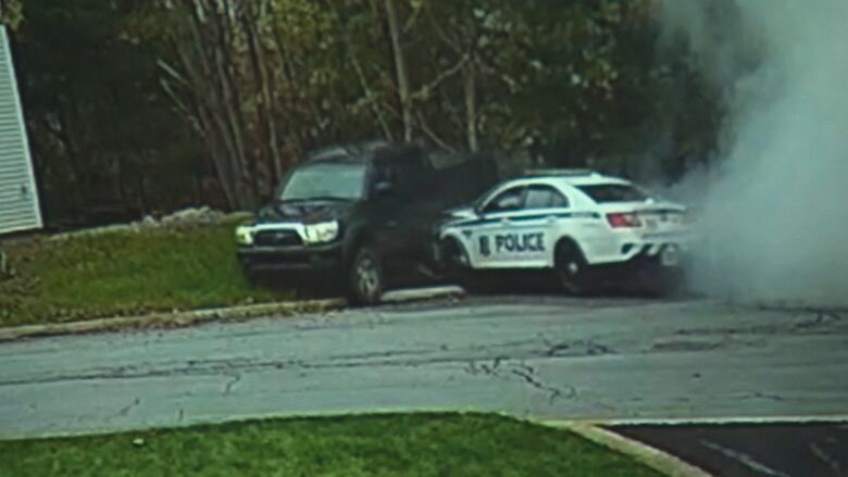 A white police vehicle is seen pushing into the driver side of a black truck. Both vehicles are on a lawn.