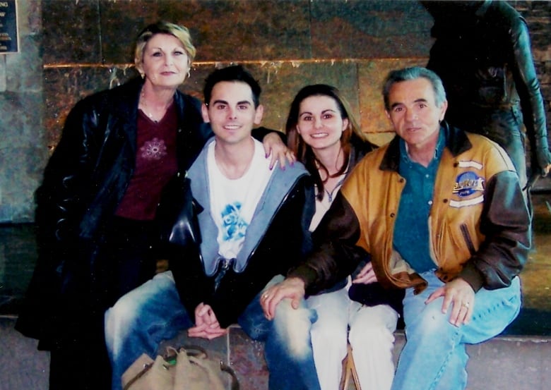 Four people sit on a bench together looking at the camera.