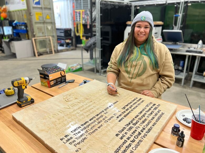 A woman smiles as she stands in front of piece of woodworking.