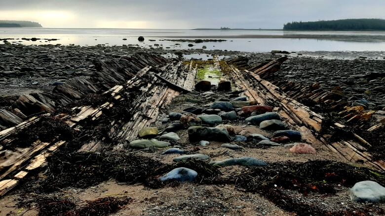 The bottom of a wooden hull spreads itself across a rocky beach heading to open water. 