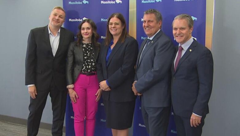 A group of people stand beside each other in front of a blue backdrop with the province of Manitoba's logo.