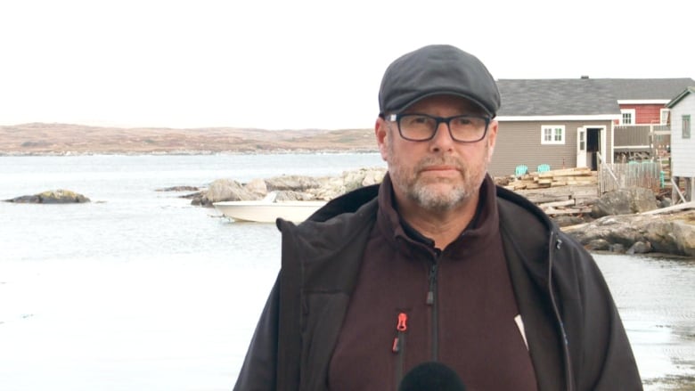 Man with hat on stands outside with serious look on face