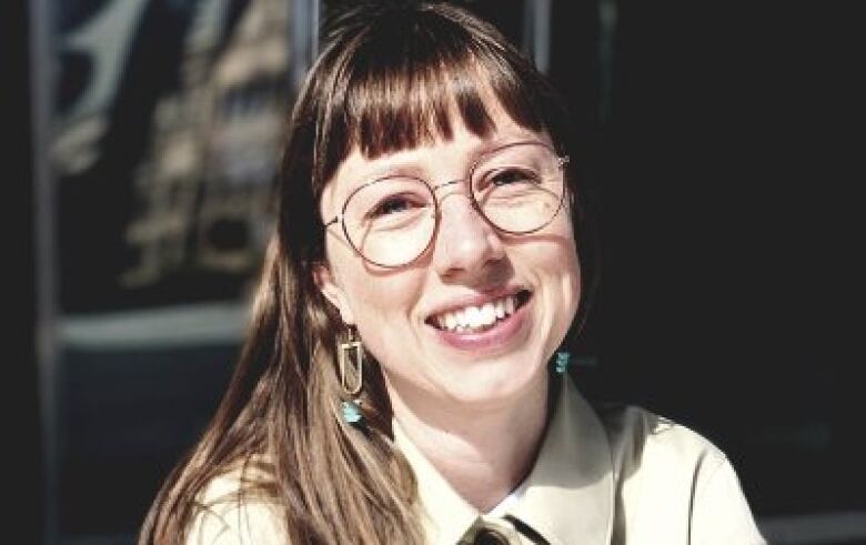 A woman wearing glasses smiles at the camera.