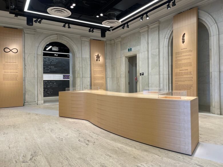 A large foyer with grey walls and floors. There's a large wooden counter in the centre and wooden panels along the walls.