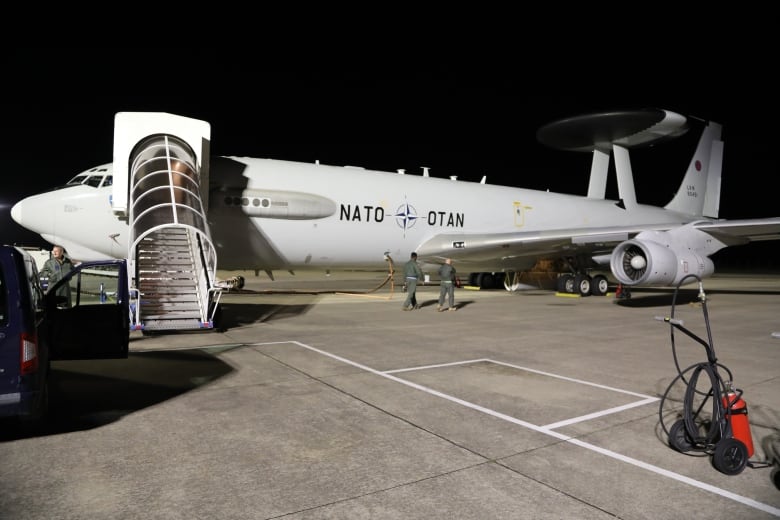 An E-3 plane with a massive radar dome mounted on top is seen at an airfield. 