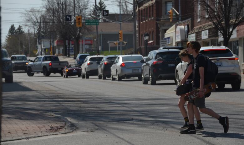 Two young people carrying skateboards walk across Whitewood Avenue in New Liskeard