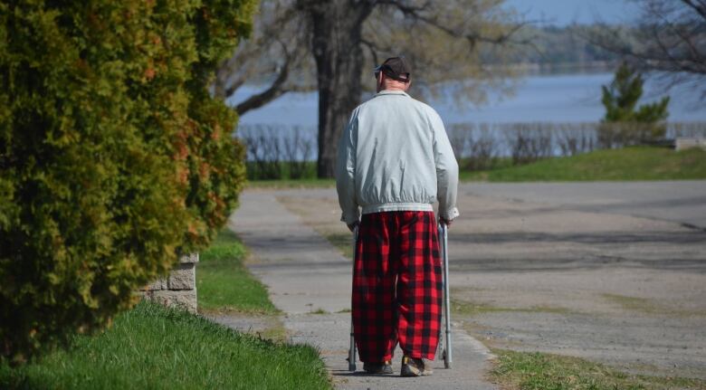 An elderly man wearing plaid pyjamas walks with walker along a sidewalk in New Liskeard.