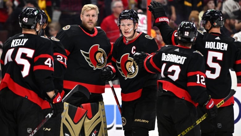 A group of hockey players gather around their goalie after a win.