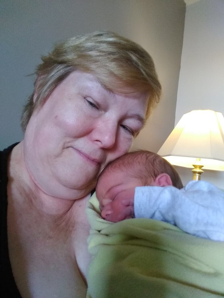 A close-up of a grandmother holding her swaddled grandchild to her neck. 