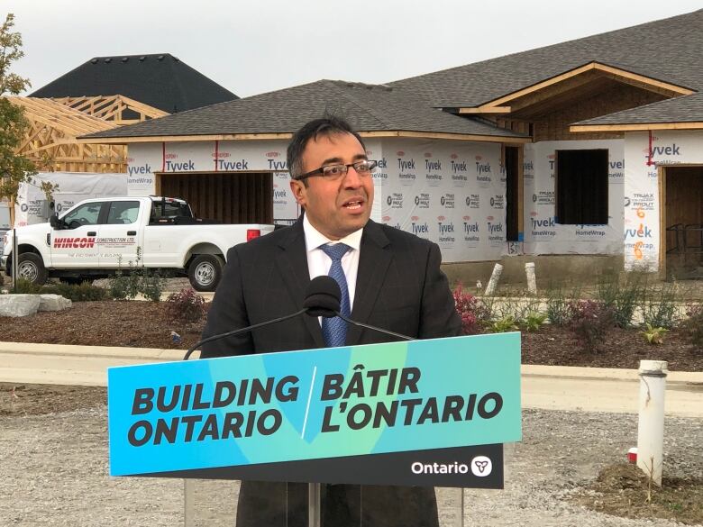 Minister Rasheed in a suit outside of a home under construction in Windsor.