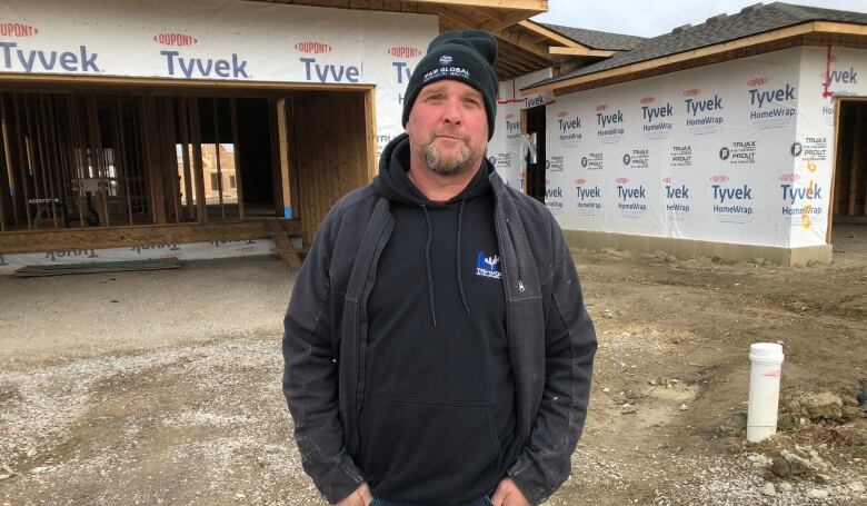 Mark Miller stands on a construction site in a sweater and hat. 