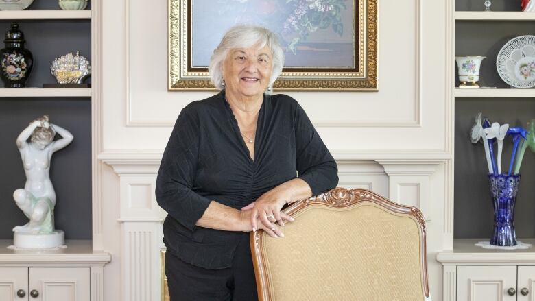 An older woman posing with her arms rested on a chair.