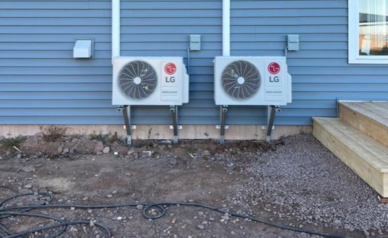 Two exterior heating and cooling units installed on the side of a home with blue siding.