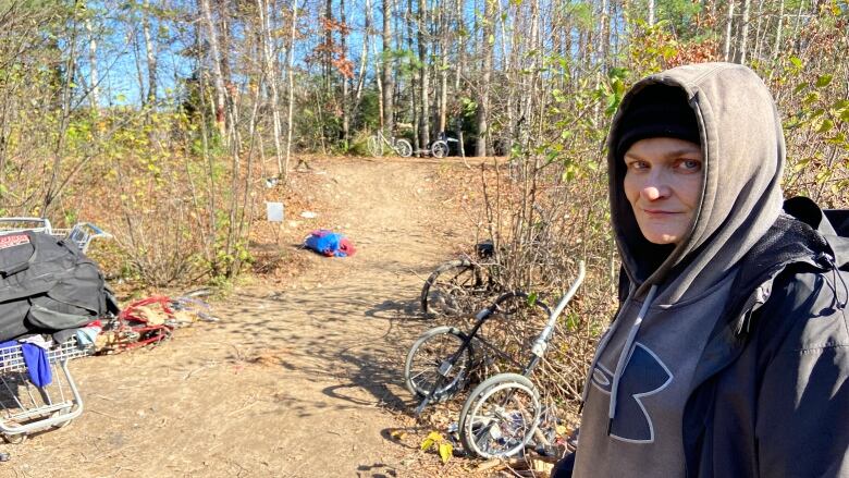 A woman stands outside in a wooded area.