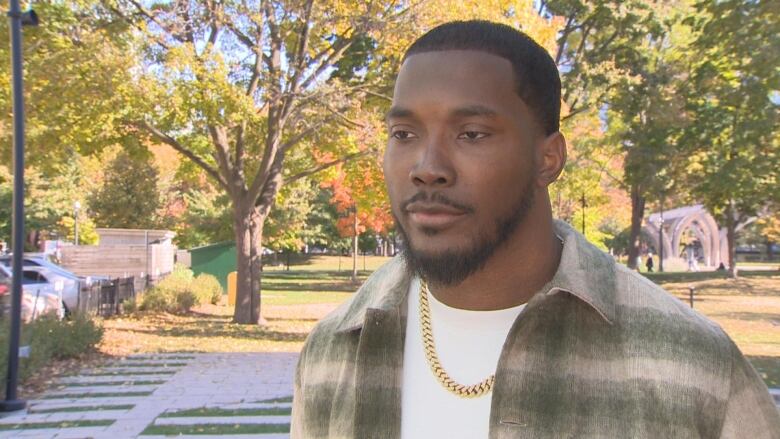 Doug Middleton, shown wearing a plaid jacket, standing in front of a park filled with colourful fall leaves. 