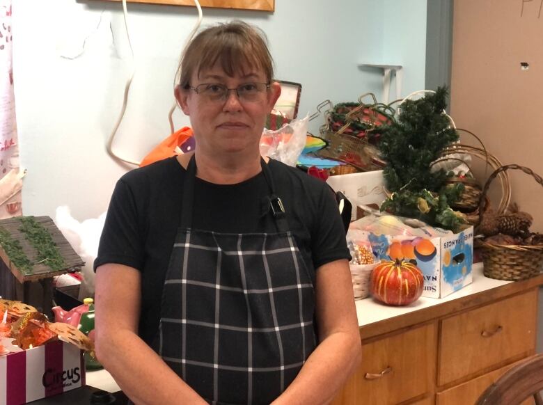 Woman wearing a black apron stands in front of a counter with craft supplies.