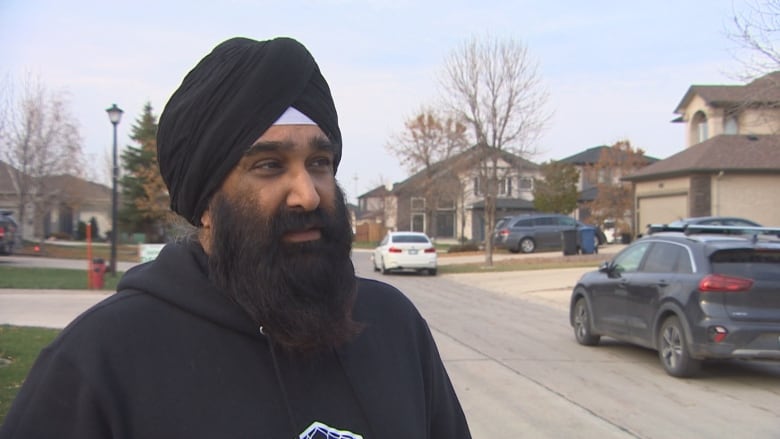 A man with a beard looks sideways with houses behind him.