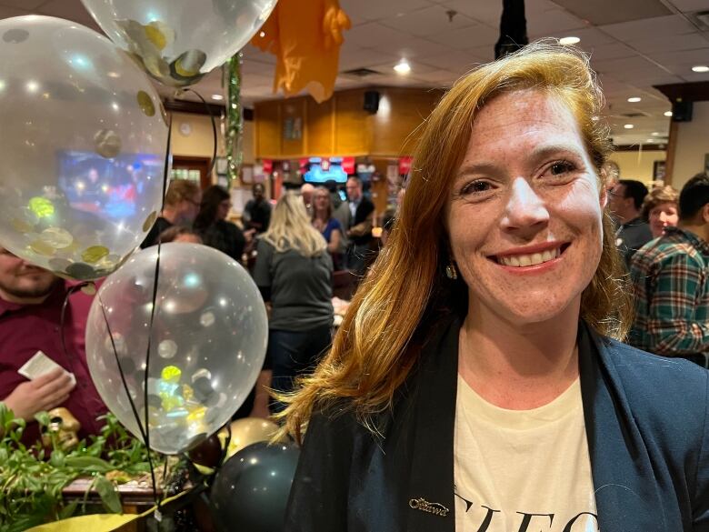 A woman smiles at the camera with balloons in background.