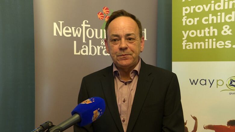 A middle-aged man with receding brown hair speaks in front of a microphone following a funding announcement.