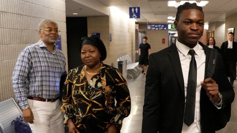 A young black man in a suit, with his mother and father in the background.