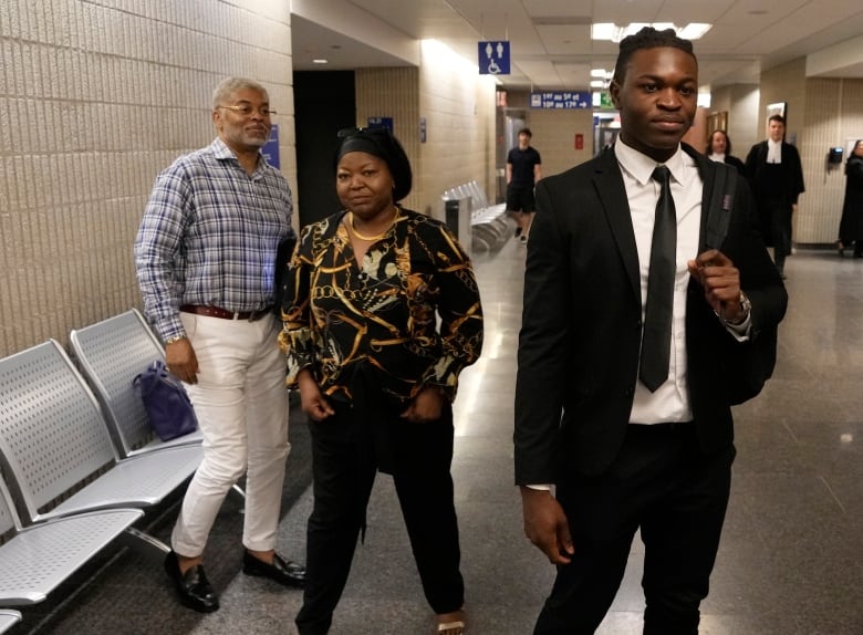 A young black man in a suit, with his mother and father in the background.