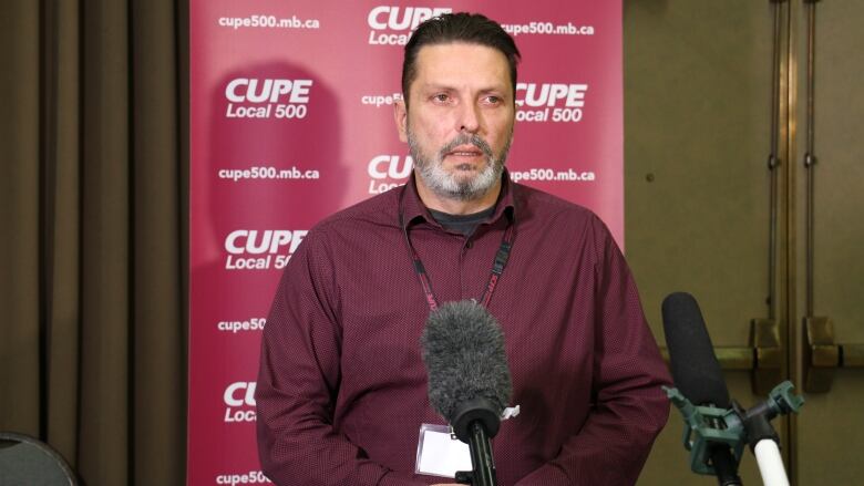 A bearded man stands in front of a backdrop reading 