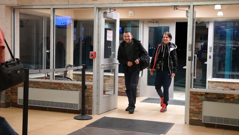 Two men walk through airport security doors. 