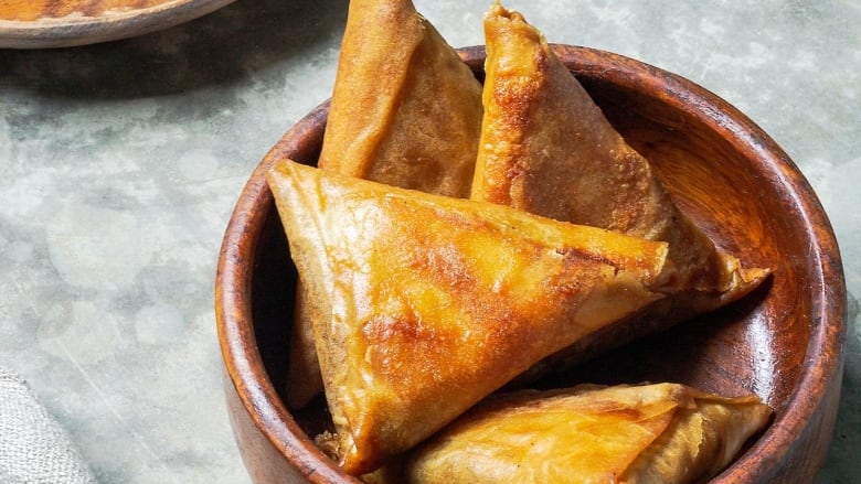 a wooden bowl of lentil samosas on a grey table.