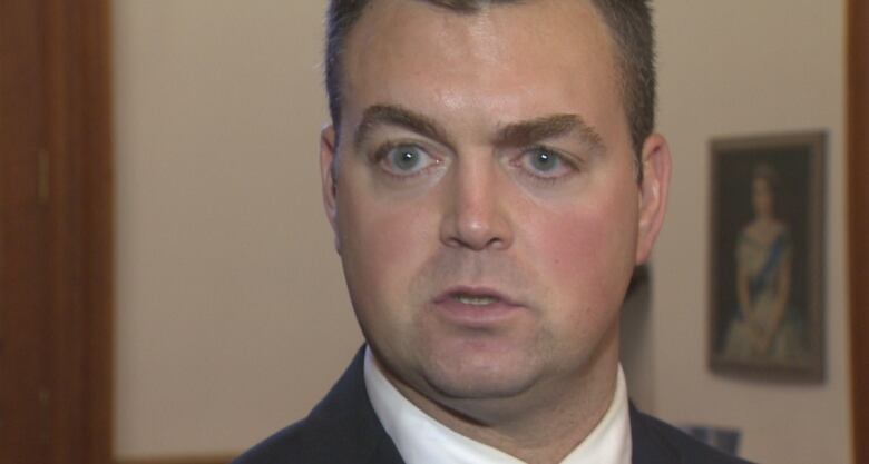 A closeup of a serious-looking man with short dark hair, wearing a suit.