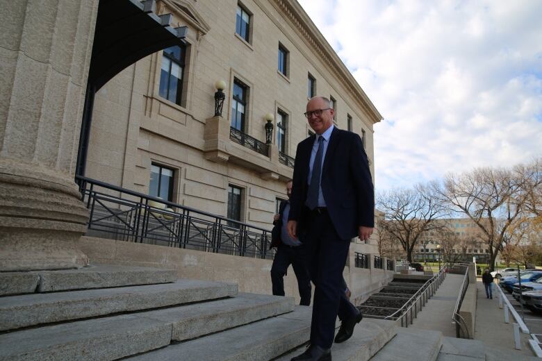 A man in a suit smiles as he walks up the steps of a legislative building.