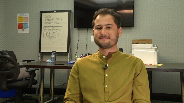 A man wearing a green shirt smiles in a conference room.