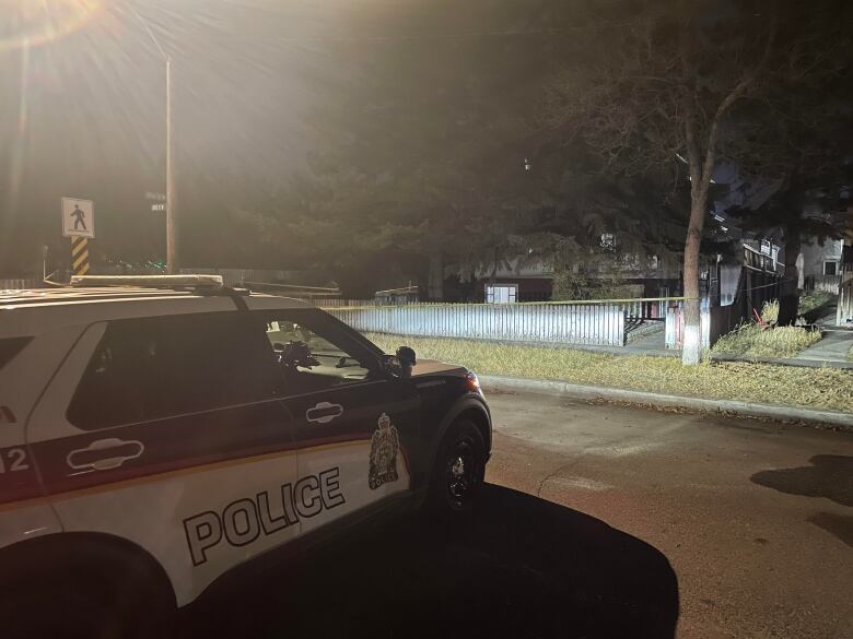 A police car outside a house surrounded by police tape.