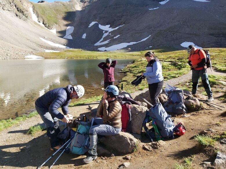 A group of people surrounded by their mountaineering equipment with the Rocky mountains in the background. 