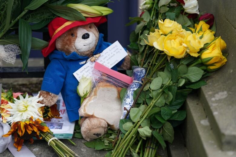 A teddy bear lies surrounded by flowers.