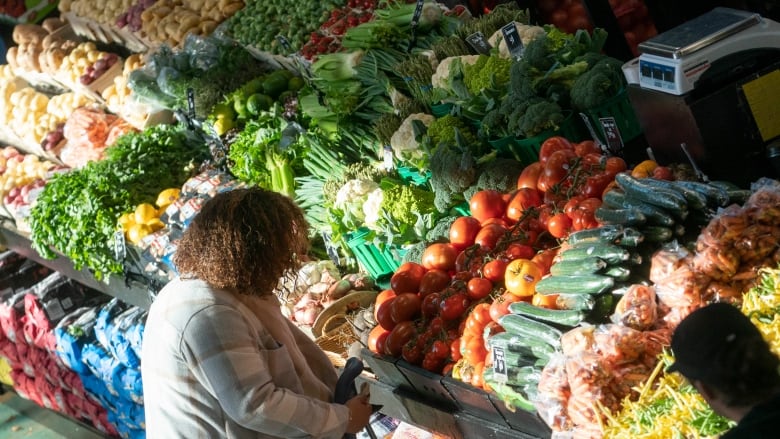 A woman, seen from behind, stands in front of abundant supply of vegetables.