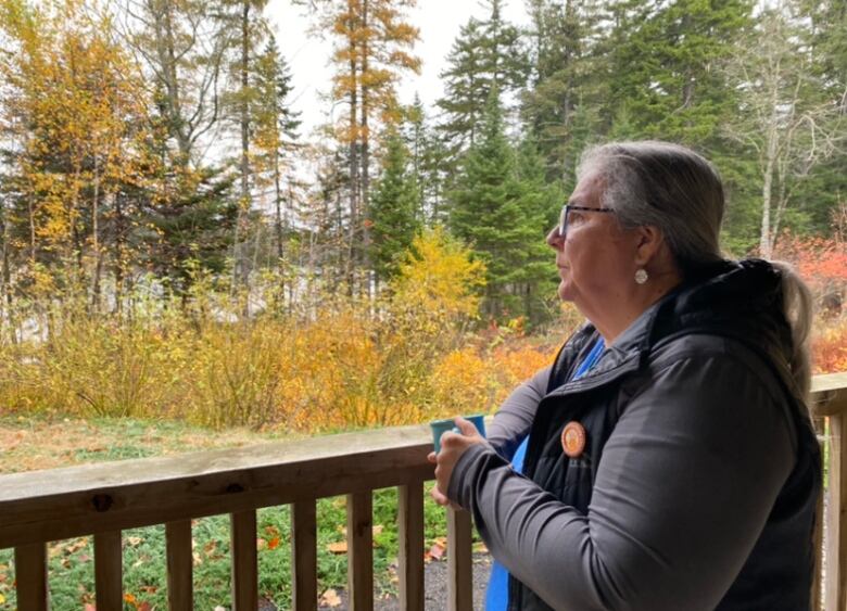 A woman sits on a porch, looking out a yard and trees.