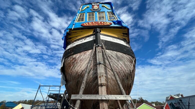 The wooden ship sits surrounded by scaffolding under a bright blue sky.