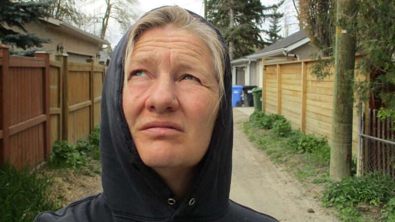 A woman wearing a hoodie goes for a walk in the neighbourhood.